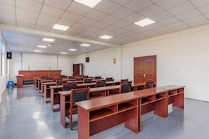 A conference room with rows of wooden tables and chairs, a podium, and a large wooden door. - Shikang Shiwai Taoyuan Leisure Tourist Resort (Guangde)