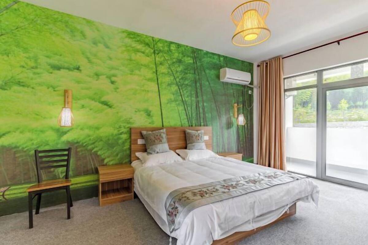 A bedroom with a bed, nightstands, a chair, a wall mural, and a large window.