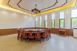 Een vergaderruimte met een ronde tafel en stoelen, grote ramen en een kroonluchter.