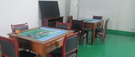 A room with a green floor, wooden tables, and chairs, a blackboard, and a white cabinet.