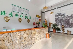Een receptiegedeelte met een stenen muur, een houten receptiebalie, groene borden, klokken en een muurschildering.