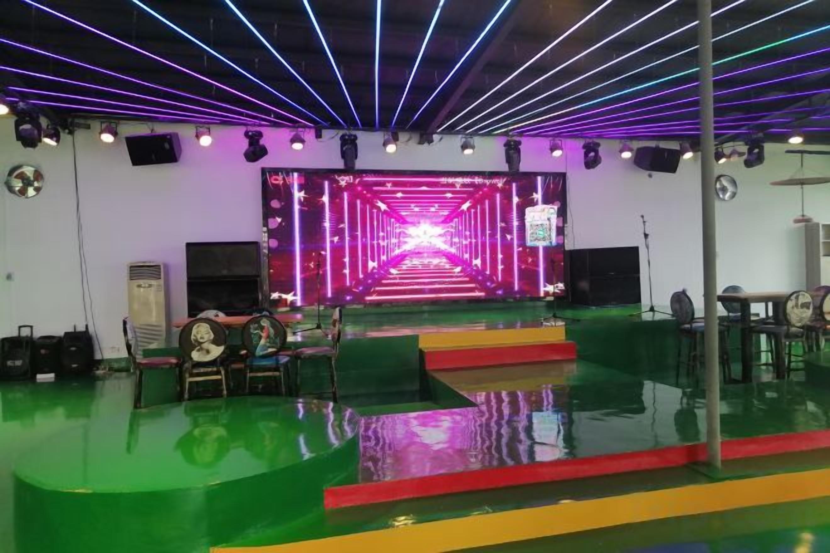 A stage with a neon-lit pathway, a green floor, and a seating area with chairs.