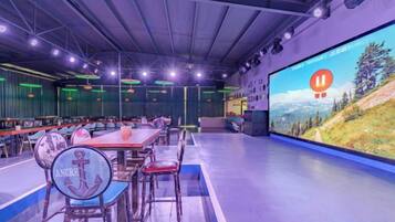 A conference room with a large screen displaying a scenic landscape, multiple tables with chairs, and a stage area.