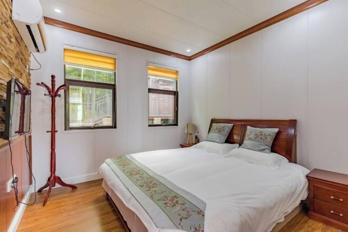 A bedroom with a bed, bedside tables, a wooden wardrobe, a standing lamp, and a window with a curtain.