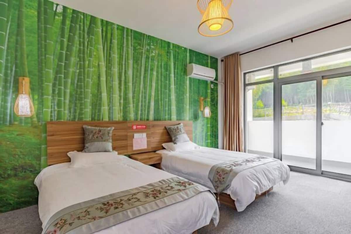 A hotel room with two beds, a green wall mural, a large window, and a ceiling light fixture.