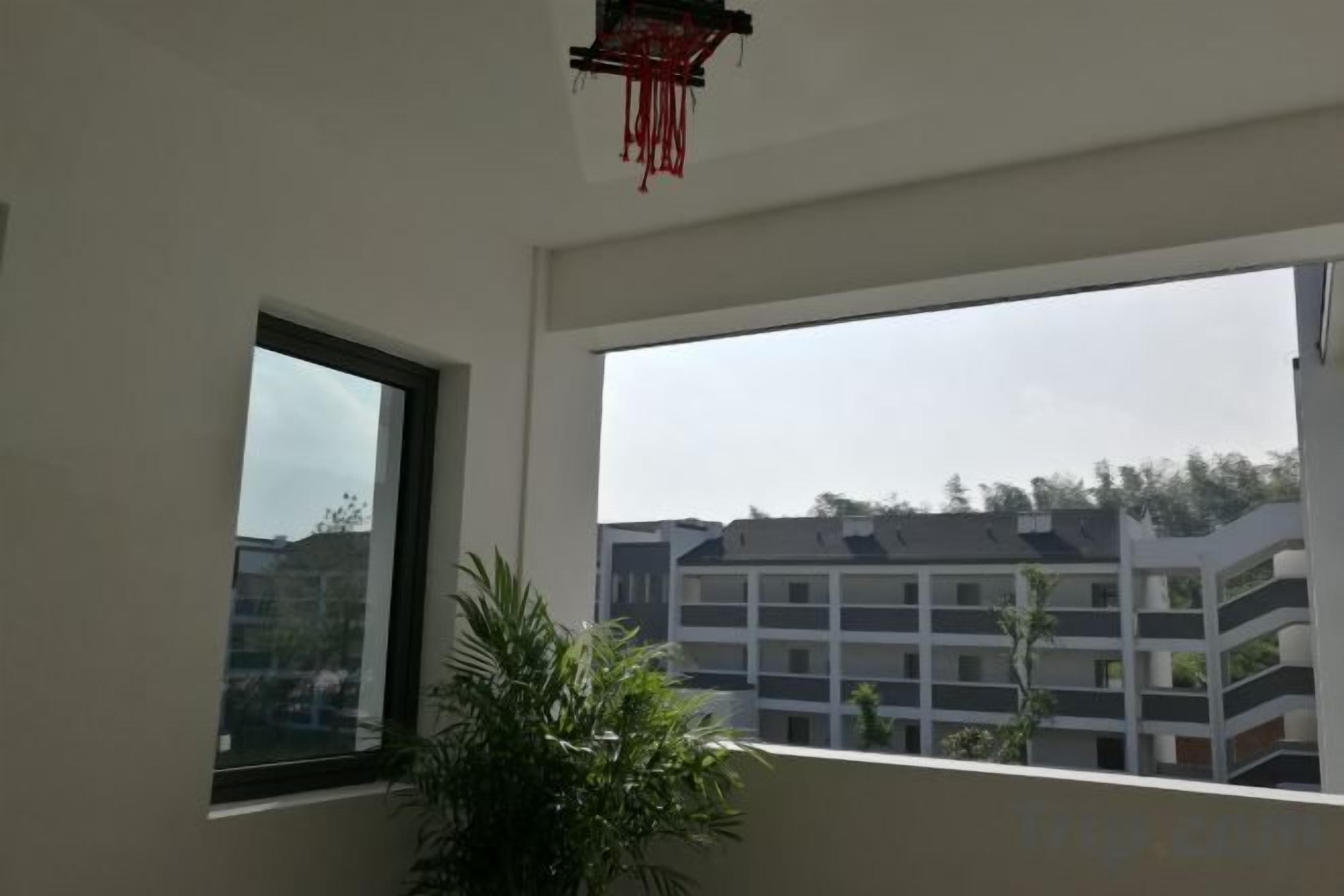 Une pièce dotée d’une grande fenêtre, d’une plante en pot et d’une décoration rouge suspendue.