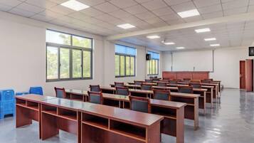 Une salle de classe avec des rangées de bureaux, de grandes fenêtres et un écran de projection.