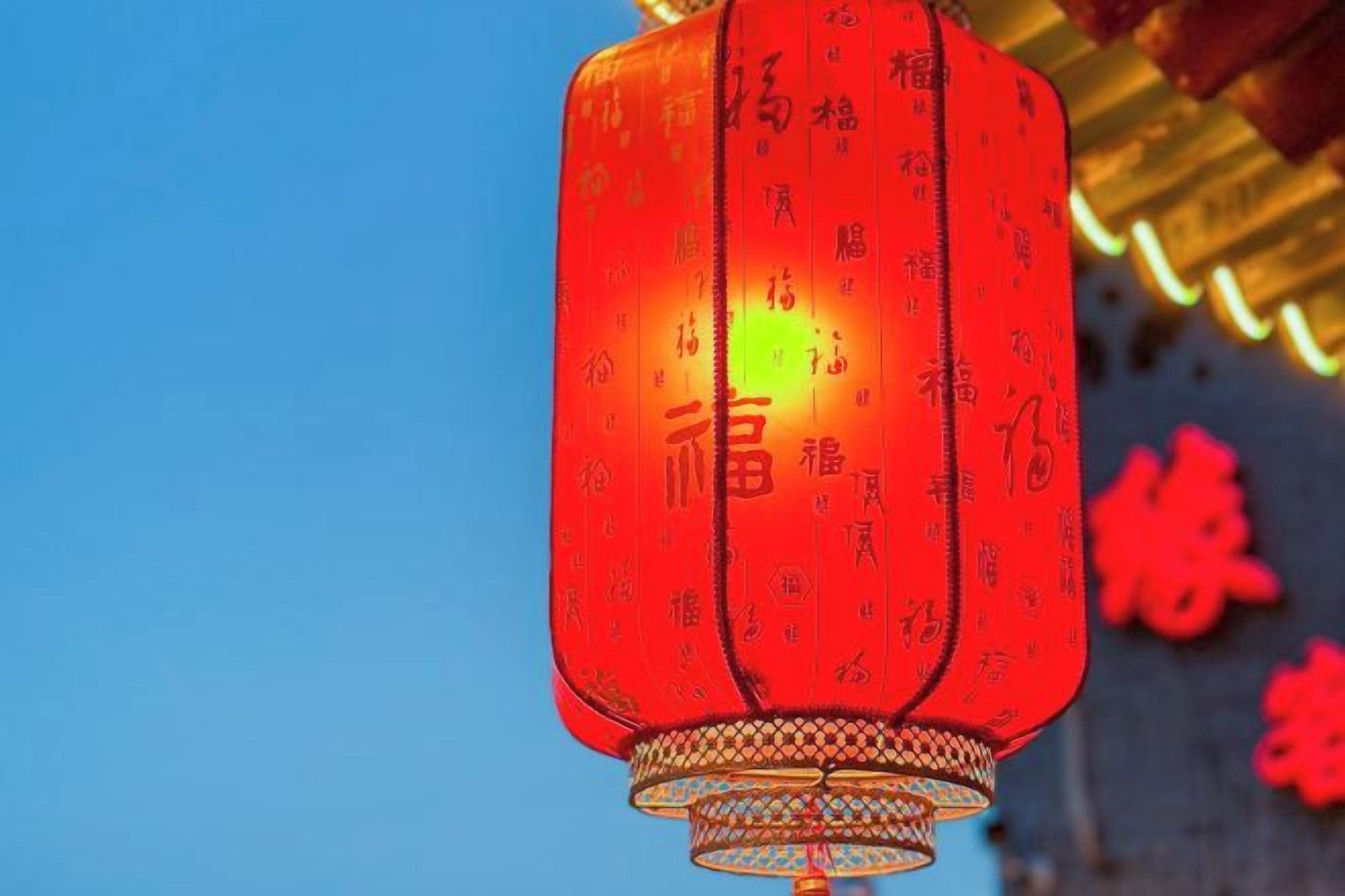 Ein roter Laternen mit chinesischen Schriftzeichen, der vor blauem Himmel hängt.
