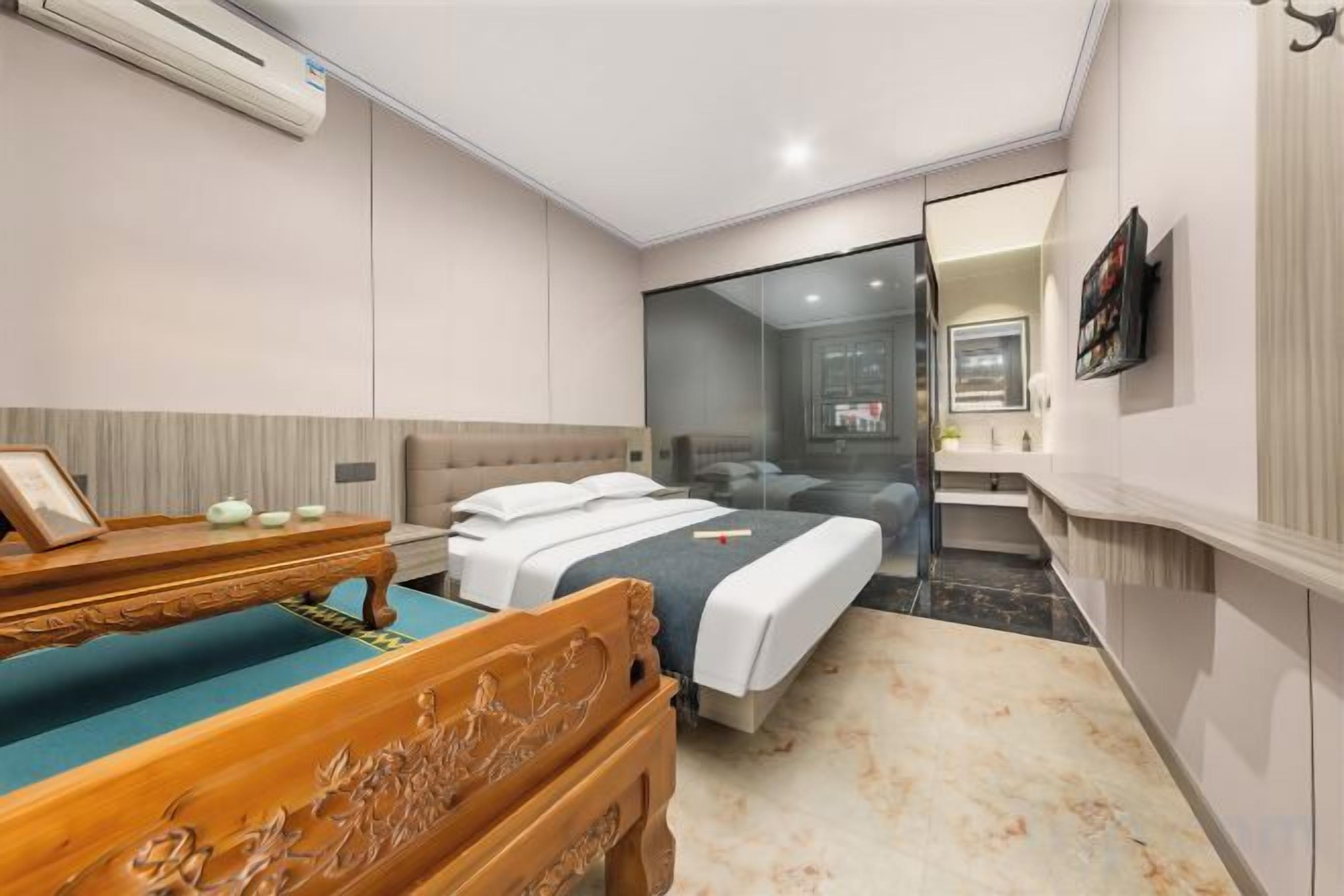 Habitación de hotel con una cama, un banco de madera, una mesita con un marco de fotos y un espejo en la pared.