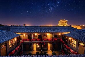 A traditional building with a tiled roof, a courtyard with a seating area, and a distant pagoda under a starry night sky. - Yuanlaiju Inn (Pingyao County)