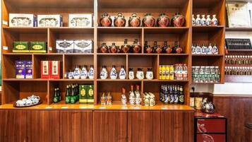 Zona de bar con estantes llenos de botellas y cajas, una barra de madera y un mueble rojo.