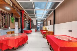 A restaurant with tables covered in red tablecloths, a glass ceiling, and a view of the street outside.