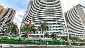 Een hotel met meerdere verdiepingen, met een gebogen gevel, balkons en een centrale binnentuin met palmbomen.