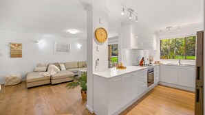A modern kitchen with white cabinets, a central island, and a large window overlooking greenery. - Shelly Cove Apartment 12 - aircon, pool, beach across road (Port Macquarie)