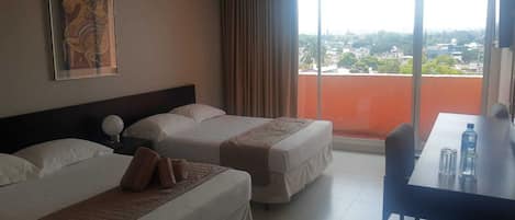 Habitación de hotel con dos camas, una mesa de comedor y un ventanal con vistas a la ciudad.