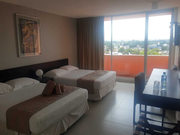 A hotel room with two beds, a dining table, and a large window with a city view.