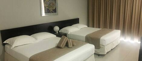 A hotel room with two beds, a headboard, a nightstand, a lamp, and a curtain.