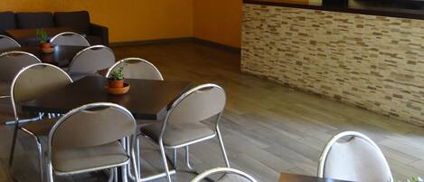 Un comedor moderno con varias mesas y sillas, un televisor de pantalla plana montado en la pared y un papel tapiz decorativo al fondo.