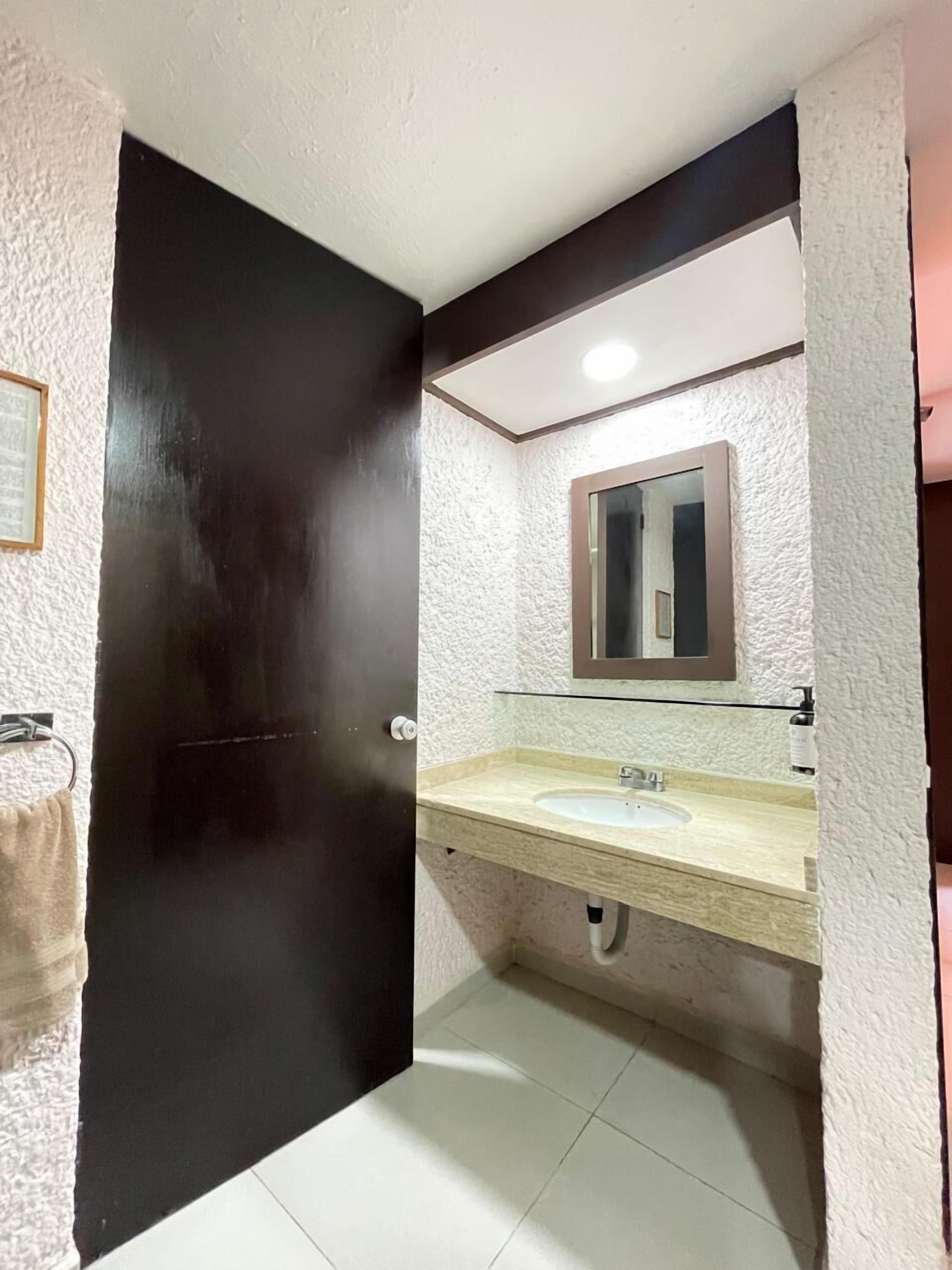 Un baño con lavamanos blanco, un espejo y una puerta negra.