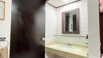 Un baño con lavamanos blanco, un espejo y una puerta negra.