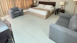 Una habitación de hotel con una cama, dos mesitas de noche, una silla, un sofá y un cuadro en la pared.