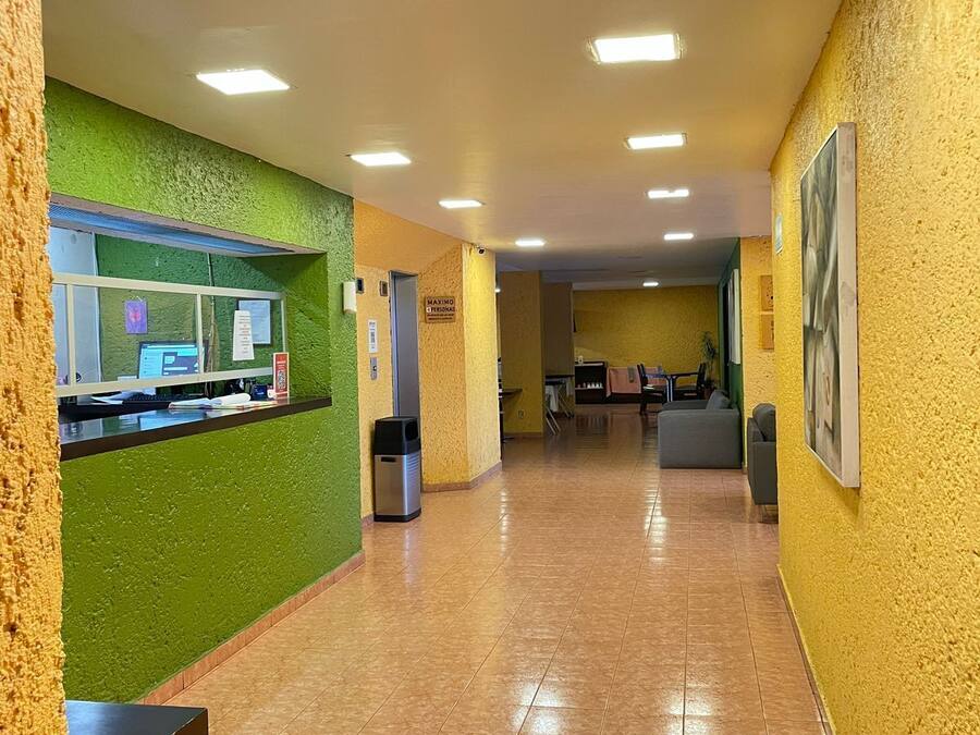 Un corridoio con pareti verdi e gialle, e pavimento piastrellato. Si nota un cestino e un cartello appeso al muro.