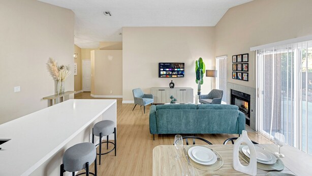 Uma sala de estar moderna com um sofá, uma mesa de jantar posta para dois e uma TV fixada na parede.