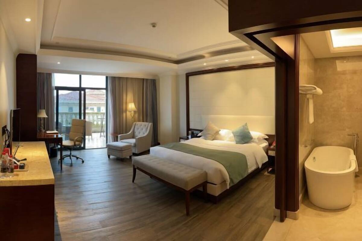 A spacious hotel room with a large bed, a sitting area with a chair, a desk, and a bathtub.