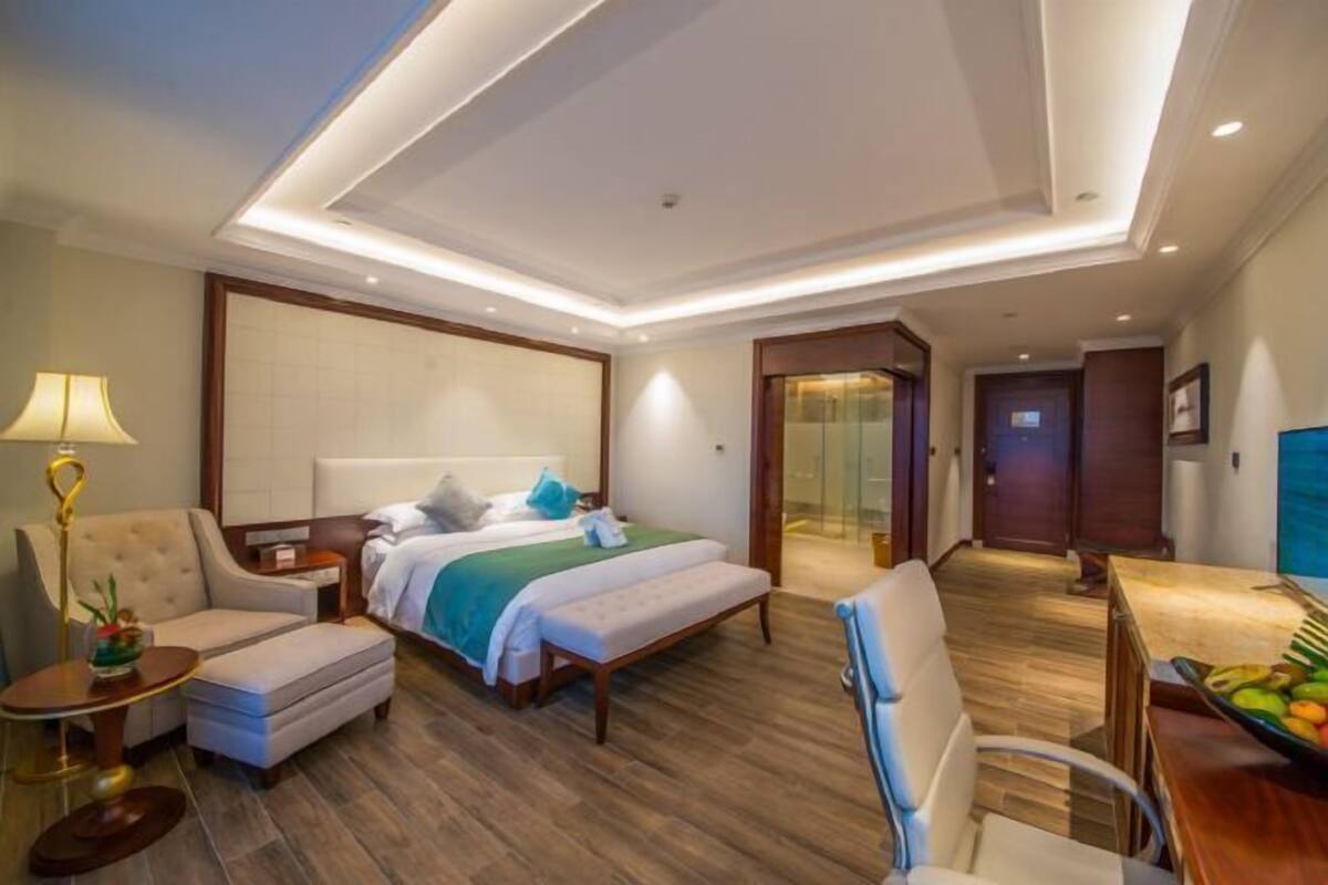 A hotel room with a bed, a desk, a chair, a small table, and a lamp.