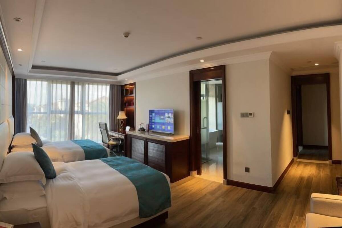 A hotel room with two beds, a desk with a TV, and a view through a glass door.