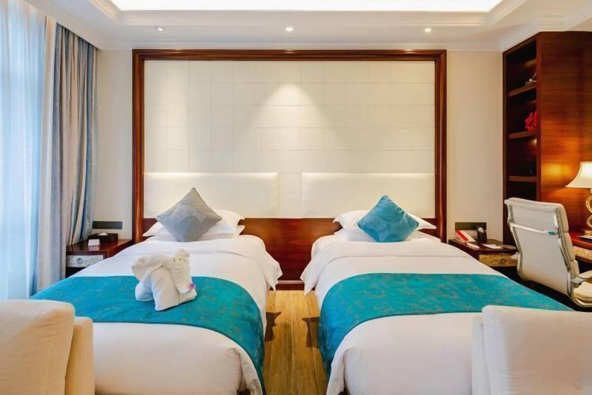 A hotel room with two beds, a wooden headboard, a desk with a chair, and a nightstand.