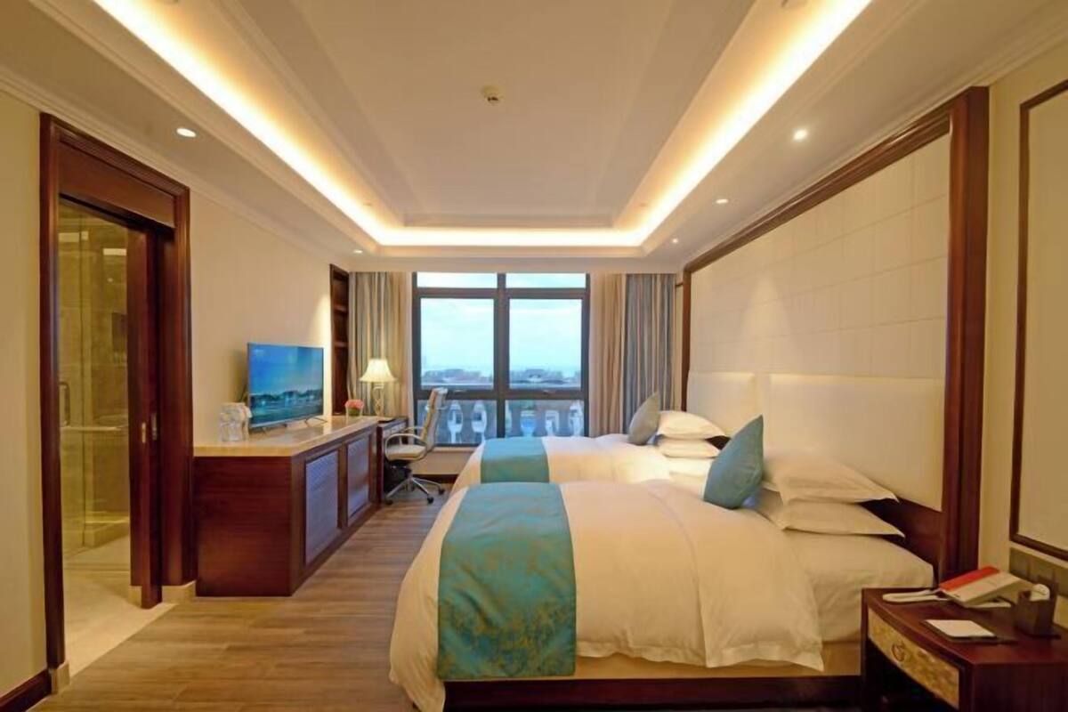 A hotel room with two beds, a desk, a TV, and a balcony view.