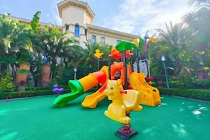 Uma área de recreação infantil com escorrega, estrutura de escalada e um brinquedo em formato de cavalo.