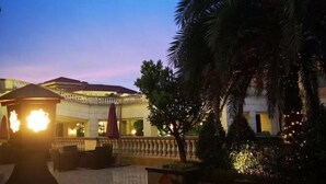 An outdoor area with a gazebo, palm trees, and a building with a balcony. - Redbird Hotel Haikou (Haikou)