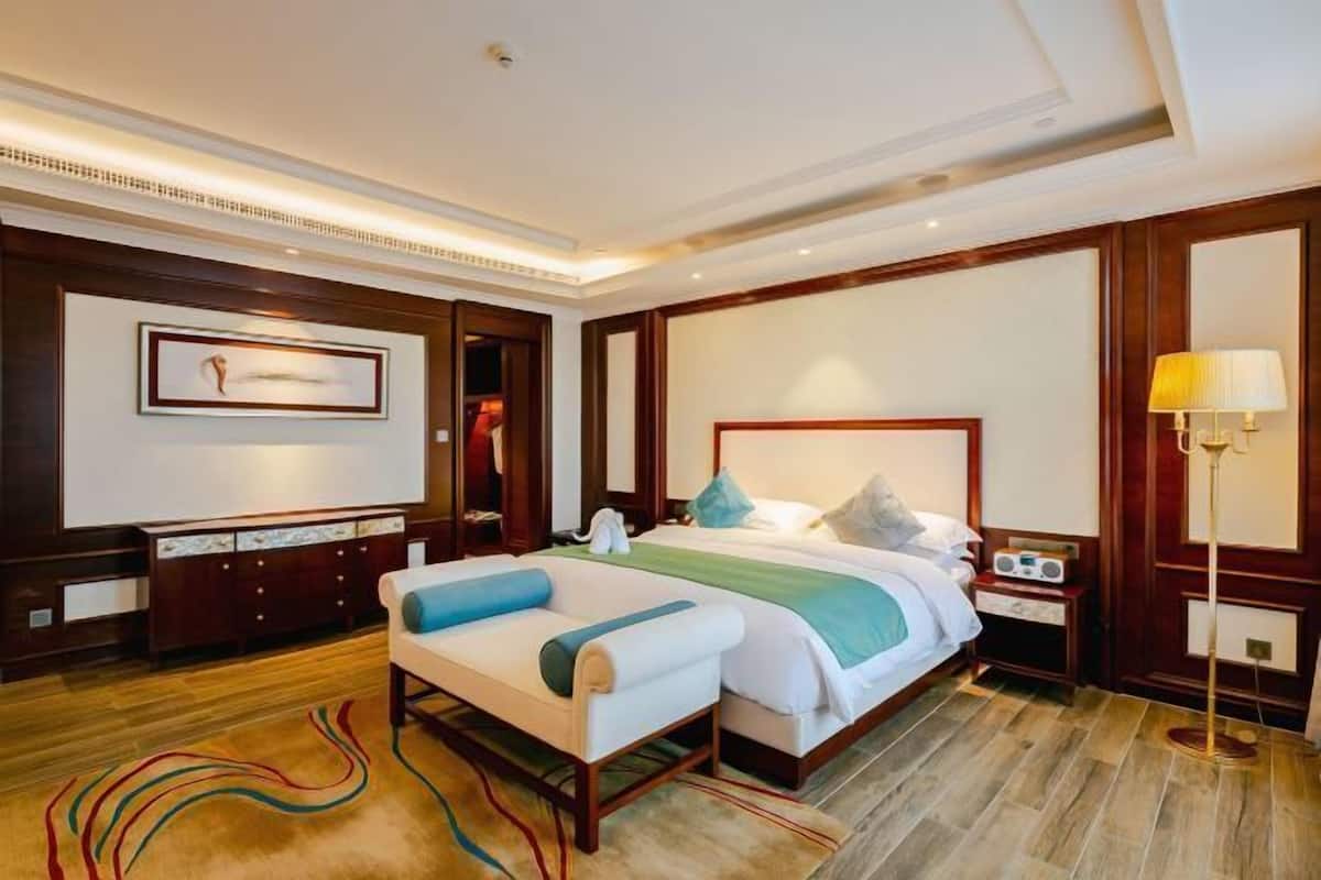 A hotel room with a large bed, a bedside table, a lamp, and a dresser.