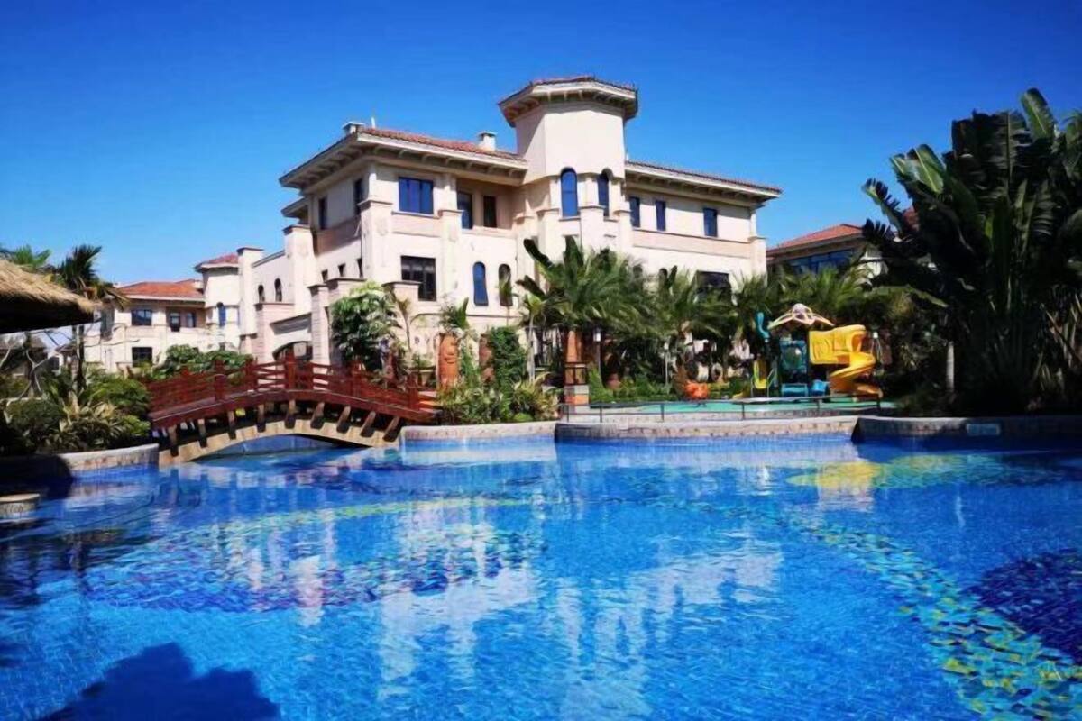 A large hotel with a swimming pool, palm trees, and a bridge.