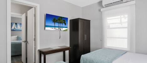 A bedroom with two beds, a wardrobe, a desk, and a painting of a beach scene.