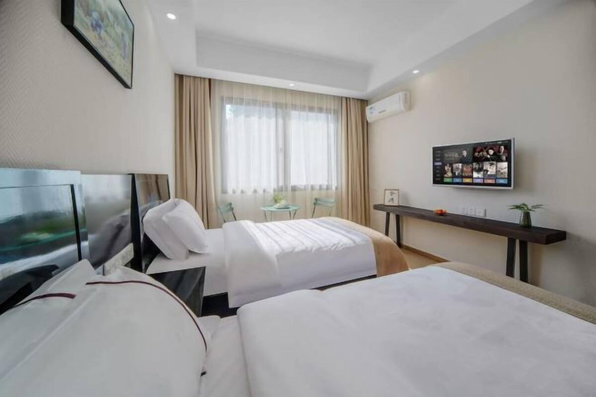 A hotel room with two beds, a TV, a desk, and a window with curtains.