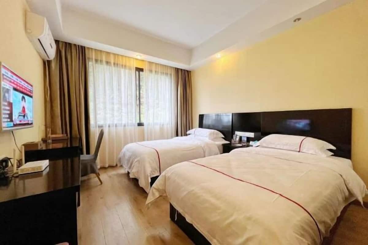 A hotel room with two beds, a desk, and a TV.