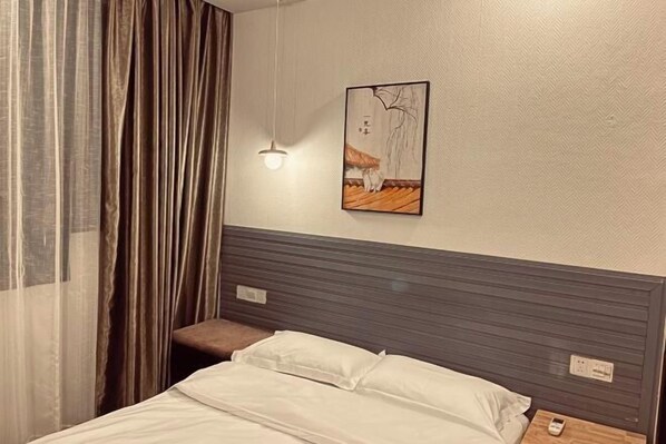 A hotel room with a bed, a bedside table, a hanging light, and a painting on the wall. - Kangyuan Villa (Wuyuan)