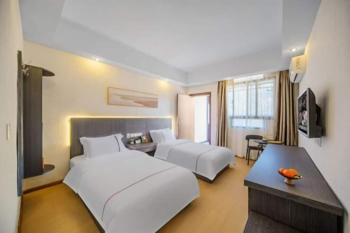 A hotel room with two beds, a desk, a TV, and a window with curtains.