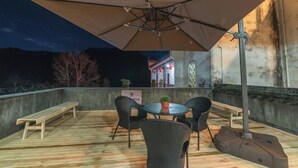 Eine Terrassengruppe im Freien mit einem runden Tisch, vier Stühlen, einer Bank und einem großen Sonnenschirm.