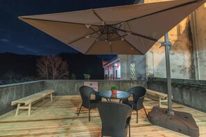An outdoor patio with a wooden deck, a round table, four chairs, and a large umbrella. - Kangyuan Villa (Wuyuan)