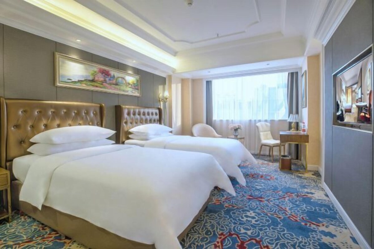 A hotel room with two large beds, a desk, a chair, and a large window.