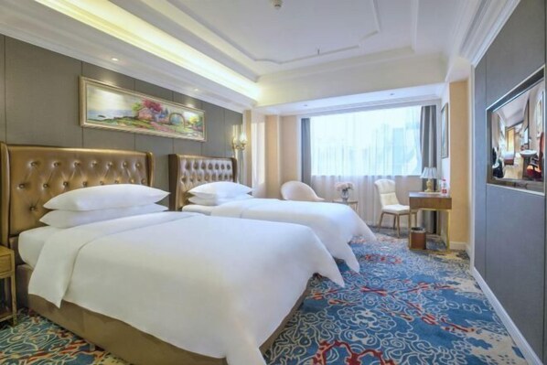 A hotel room with two large beds, a desk, a chair, and a large window.
