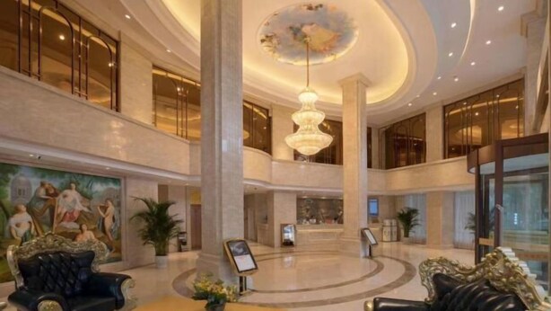 A spacious lobby with ornate black leather sofas, a central chandelier, and a large mural on the wall. - Vienna Hotel (Ziyang)