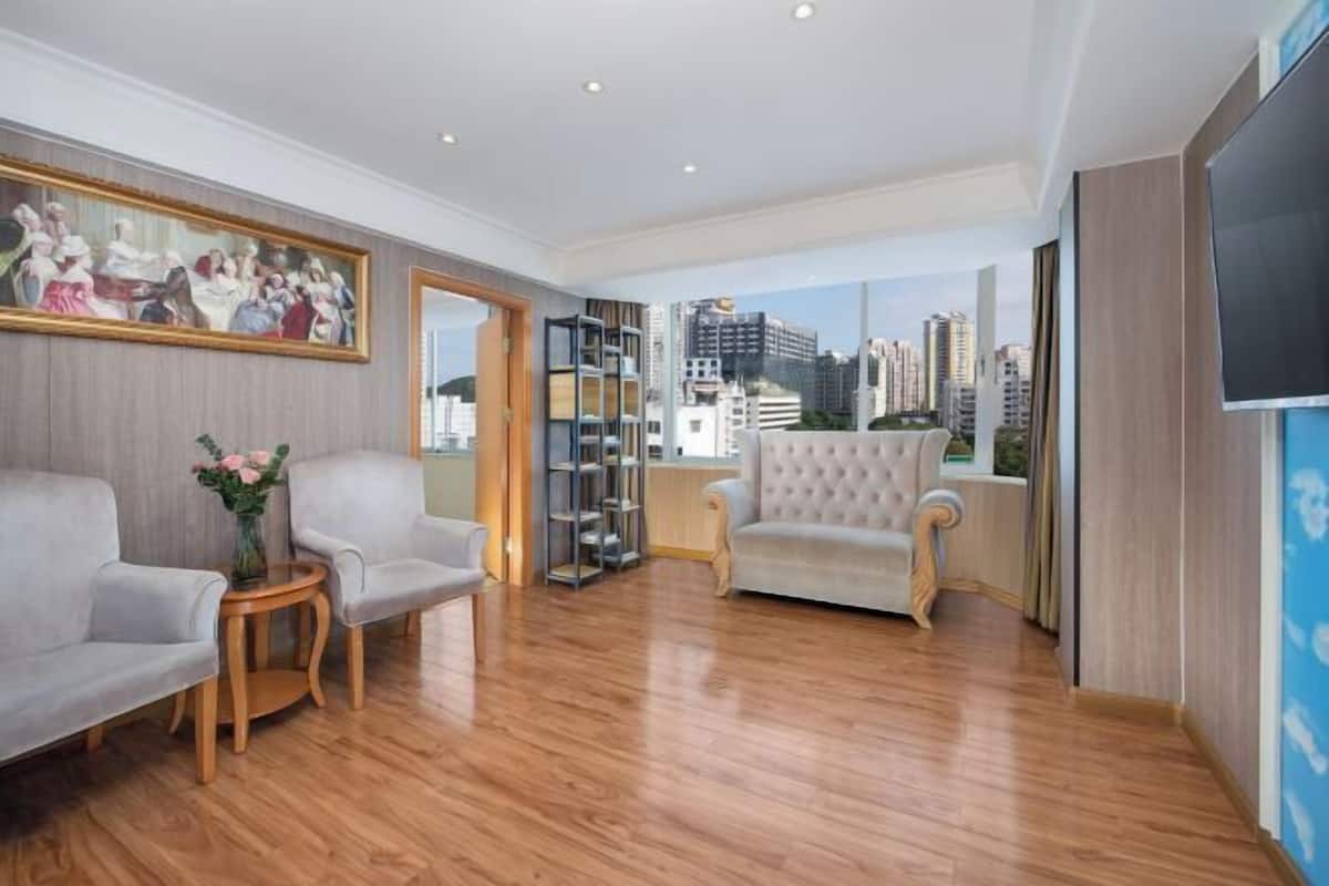 A spacious living area with a wooden floor, a large painting on the wall, a sofa, a chair, and a bookshelf.
