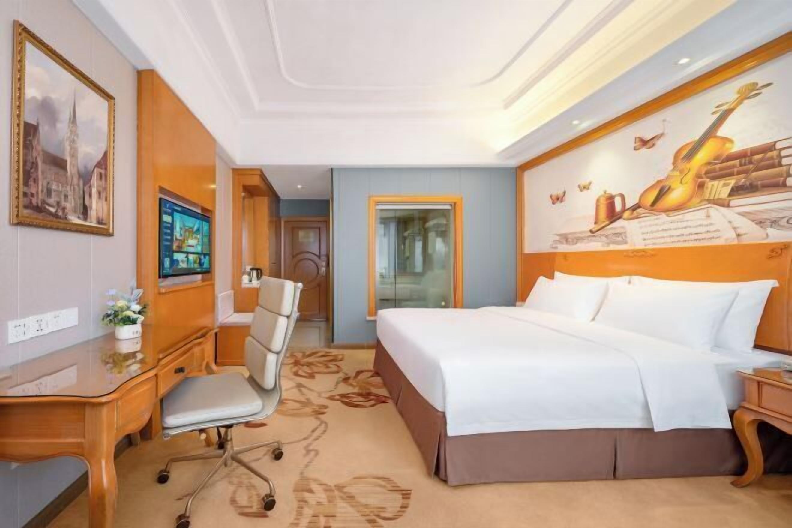 A hotel room with a bed, desk, chair, and a wall with a mural.