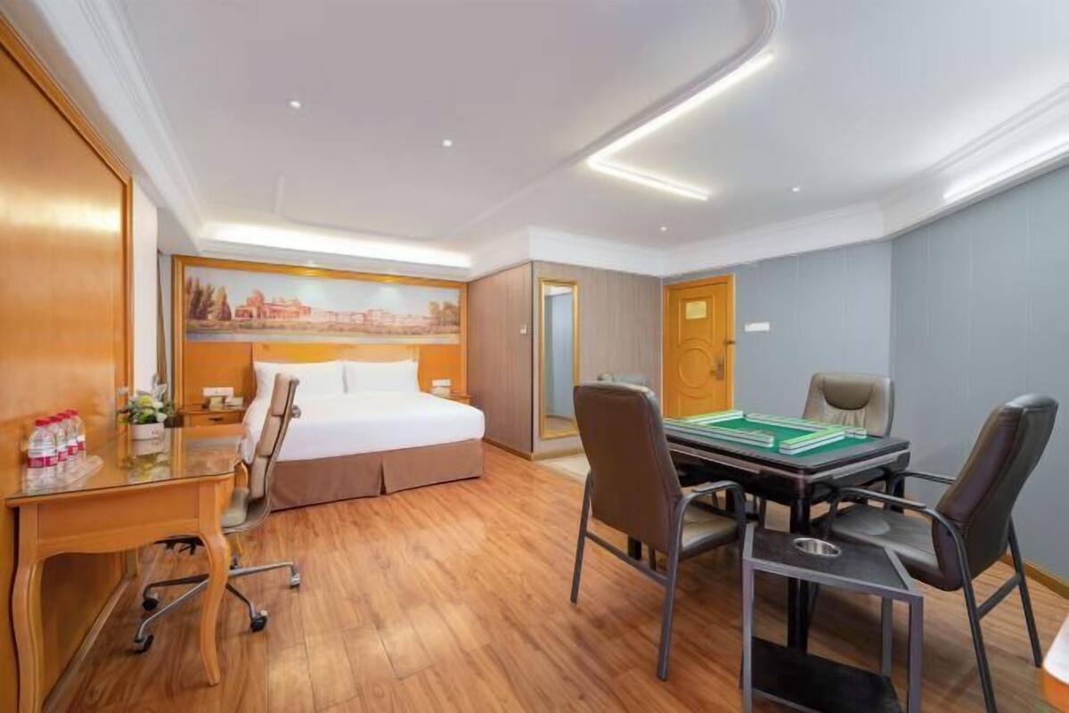 A hotel room with a bed, desk, chairs, and a table with books.