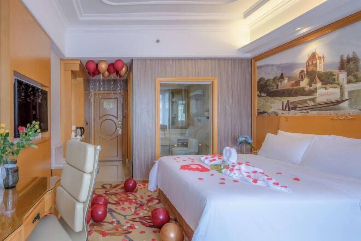 A hotel room with a bed, a desk, a chair, and a painting on the wall.